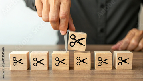 Cutting Costs: Businessperson's Hand Severing Wooden Blocks with Scissors Icon, Budget Reduction Concept