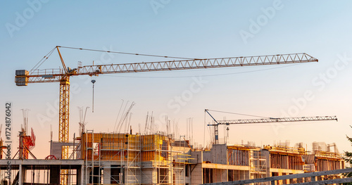 Cranes overseeing a new building site, indicating urban growth and real estate development. Modern apartments are under construction