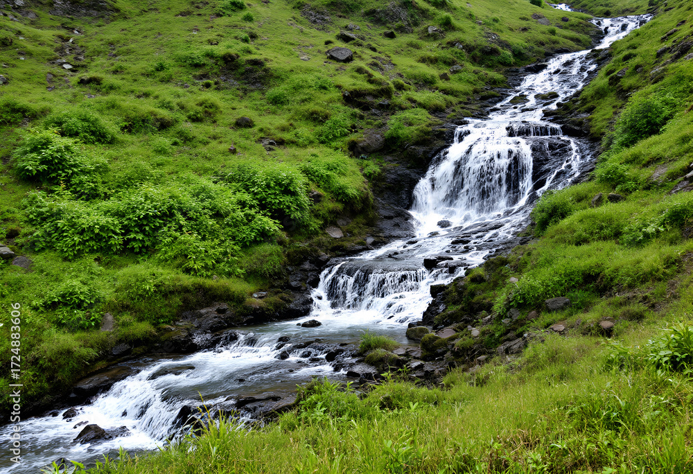 Naklejka premium Cascading Waterfall Through Lush Green Hills
