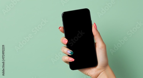 Stylish woman holding phone with blank black screen displaying trendy nail art against a modern green background, perfect for app mockups