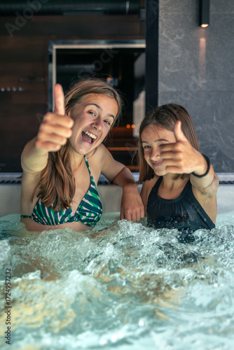 Two girls in jacuzzi with thumbs up, laughter and splashes. Family spa chill.