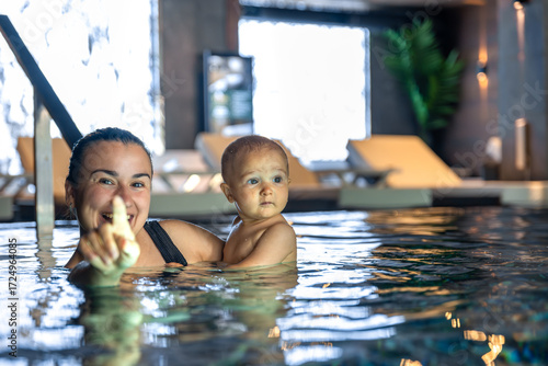 Mom pointing out to baby in warm spa pool, joyful moment. Pointing hand in frame.