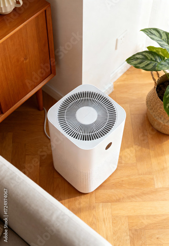 A white air purifier stands on a wooden floor next to a plant.