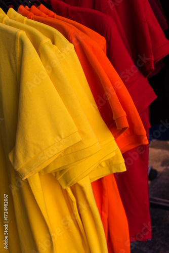 Yellow and Orange T-shirts hanging on Hangers.