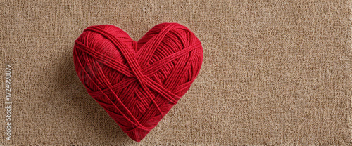 Red yarn heart on carpet background. Heart shape made of knitting yarn. Cozy love symbol with red wool ball heart. Warm red yarn heart symbolizing love.
