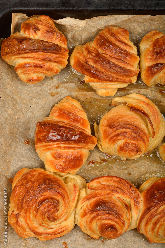 Fototapeta premium A detailed top-down view of a baking sheet filled with freshly baked, golden croissants and spiral pastries