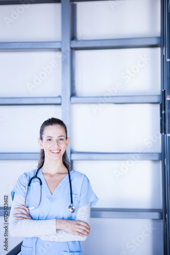 Female nurse standing before frosted glass panel with metal beams wearing blue scrubs stethoscope