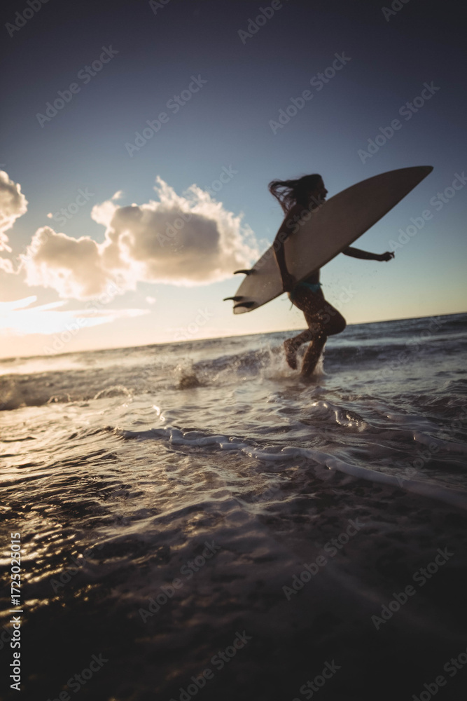 Naklejka premium Long white surfboard leaning against gentle waves as warm sunset light sparkling on wet sand