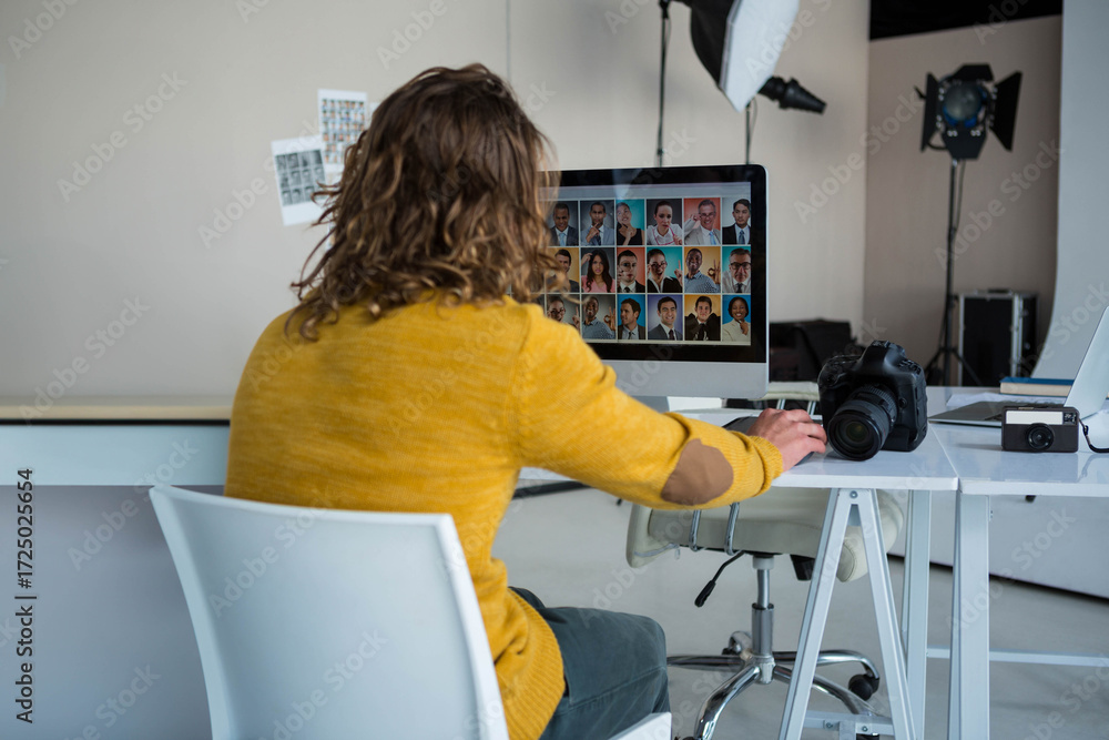 Fototapeta premium Widescreen monitor displaying headshot grid on desk in studio, with DSLR and compact cameras