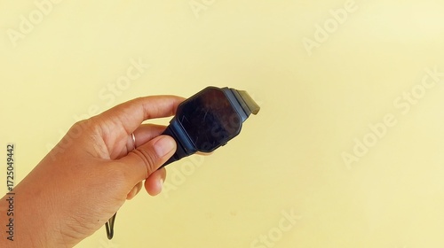 a woman's hand holding a black watch on a yellow background