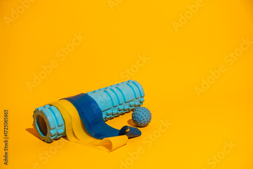 Foam roller with resistance bands and massage ball on vivid yellow background wellness recovery copy space. High quality photo
