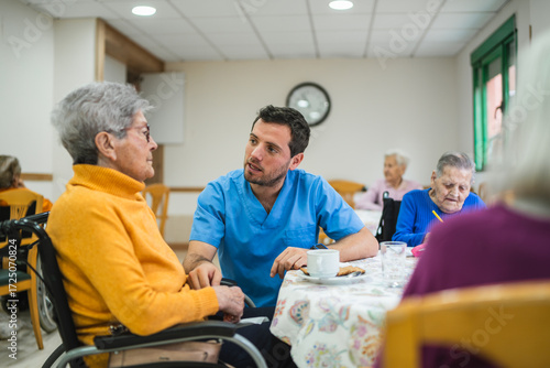 Young male caregiver providing assistance and talking with an elderly woman in a wheelchair during an activity at a retirement home