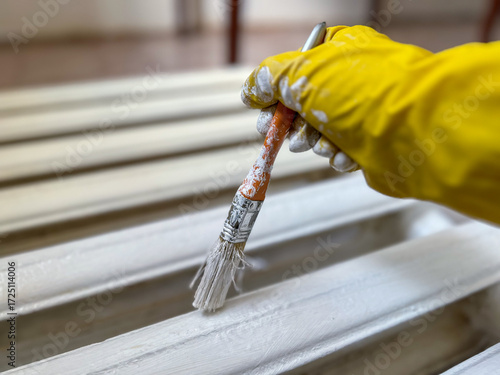 Worker hand painting old radiator with white paint using brush