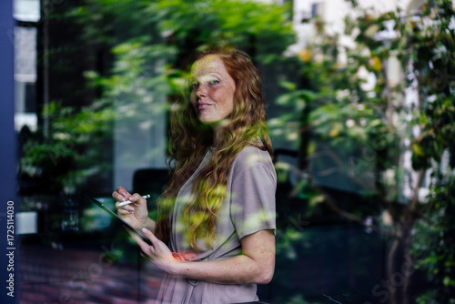 Smiling freelancer with tablet PC seen through glass window