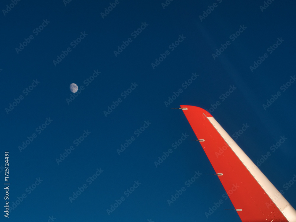 Obraz premium An aerial view from an airplane window, capturing the winglet against a deep blue sky with the moon visible in the distance.