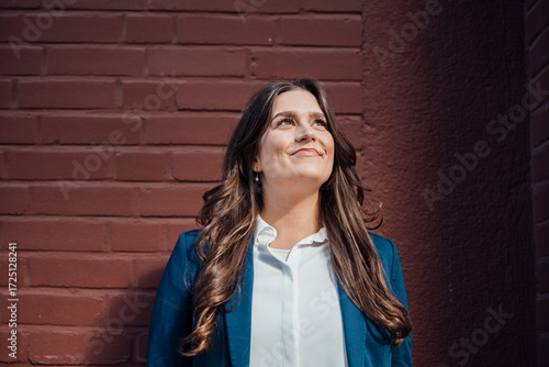 Confident businesswoman in blazer standing outdoors by brick wall