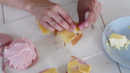 A woman prepares delicious sandwiches with cheese, butter, and sausage in a sunny kitchen. Authentic cooking process showcasing simple, comforting food preparation