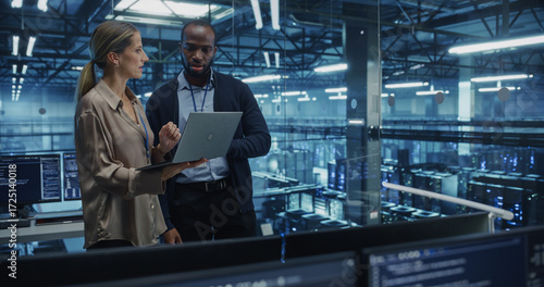 Male Cloud Architect and Female Database Engineer Review Data Storage Protocols on a Shared Laptop in a Data Center. Team Strategizing Ways to Improve Service for Enterprise Clients