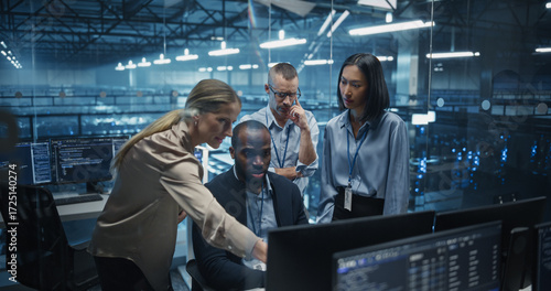 Diverse Team of IT Professionals Gathered Behind a Desk, Looking at Data on Computer Screens, Problem Solving a Data Security Project, Brainstorming Future Upgrades for Cloud Computing System