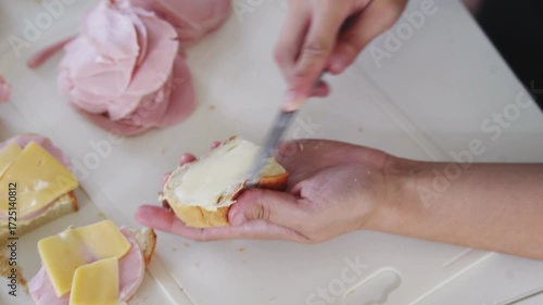A woman prepares delicious sandwiches with cheese, butter, and sausage in a sunny kitchen. Authentic cooking process showcasing simple, comforting food preparation