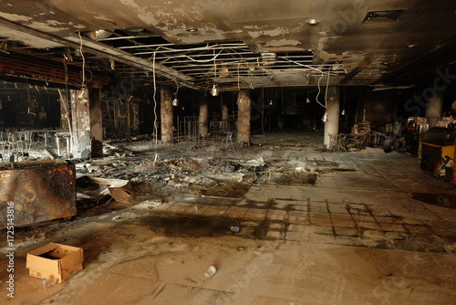 Burnt interior shows devastation after fire in commercial building, revealing charred debris and structural damage with somber atmosphere.