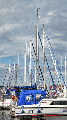 Sailing boats sit in a bay on a sunny day under a cloudy sky.