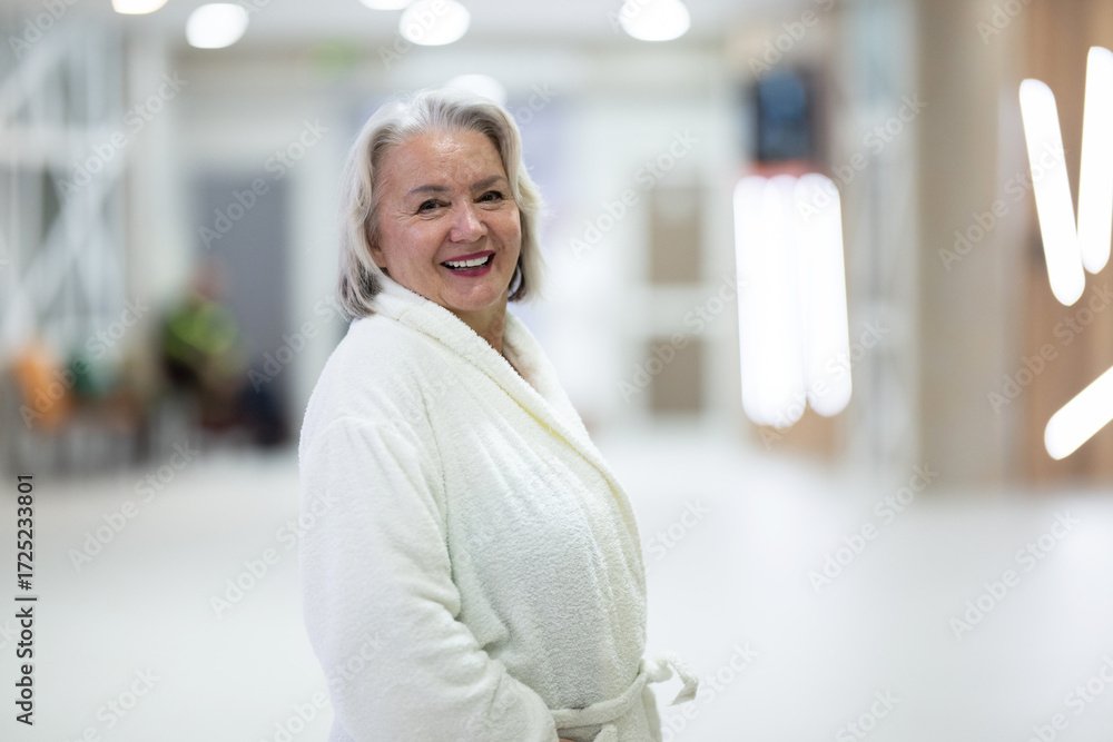 Fototapeta premium Portrait of a senior woman wearing a white bathrobe at a wellness center, symbolizing relaxation, self-care, and healthy aging lifestyle.