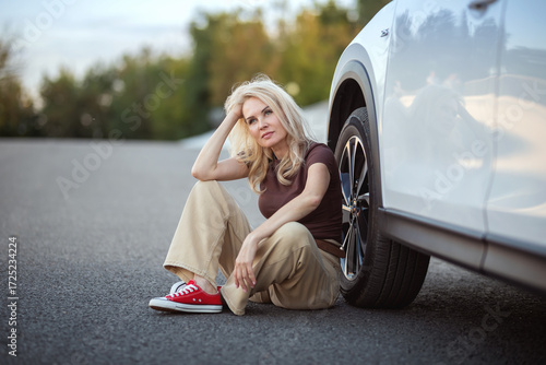 A woman is sitting on the side of the road next to a car. Travel and tourism.
