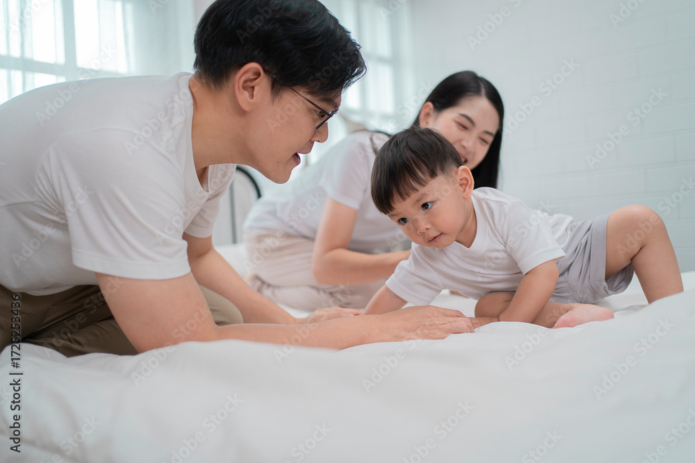 Fototapeta premium Asian family moment at home, smiling mother holding toddler boy who reaches out to father with curiosity and joy. Concept of parenting, bonding, love, and early childhood development.