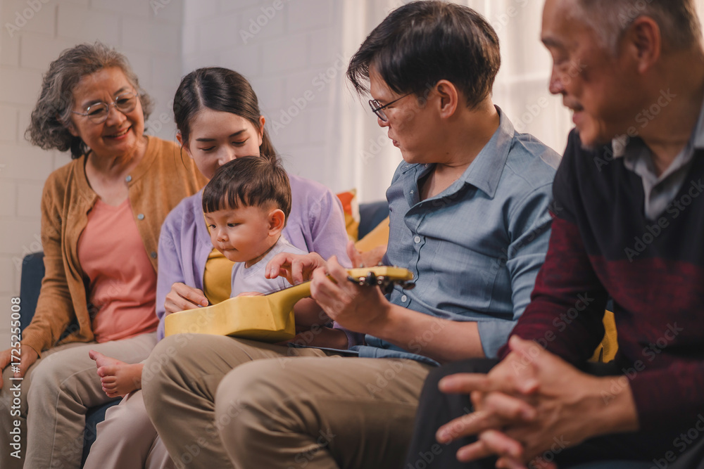 Fototapeta premium Asian multigenerational family sitting together on sofa, parents holding baby while grandparents smiling with love, concept of family bonding, parenting, childcare, affection, and happy lifestyle.