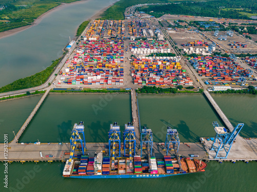 Aerial view of a bustling port with colorful shipping containers stacked high, cranes poised, and a cargo ship ready for departure at Jawaharlal Nehru Port Trust (JNPT) in Navi Mumbai, India