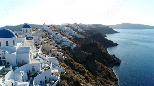 A breathtaking aerial view of the iconic white buildings and bluedomed churches of oia clinging to the cliffs of santorini, greece, overlooking the aegean sea on a sunny day