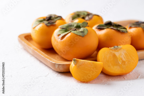 Fresh ripe persimmon on wooden plate with white background, Autumn sweet fruit