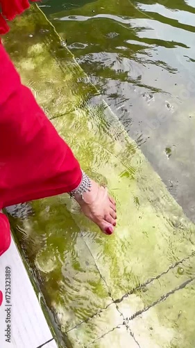 A Bengali woman wearing red sharee and anklet as she is playing with bare feet in water in Dhaka, Bangladesh