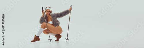 Woman in faux fur jacket and bikini posing with red skis and poles in modern studio setting. Concept of fashion advertising, bold editorial, winter lifestyle branding, and stylish campaigns. Banner
