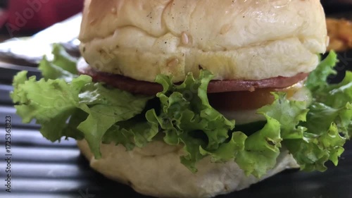 Close-up shot of a fresh hamburger with lettuce, meat slice, and fluffy sesame bun, showing its juicy texture and appetizing detail.