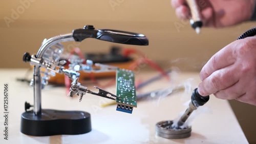 Close-up of hands soldering a printed circuit board with a soldering iron in a workshop. Concept of electronics repair, technology, DIY, and microchip maintenance.