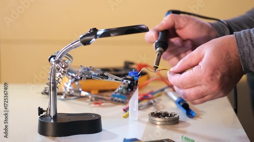 Close-up of hands soldering a printed circuit board with a soldering iron in a workshop. Concept of electronics repair, technology, DIY, and microchip maintenance.