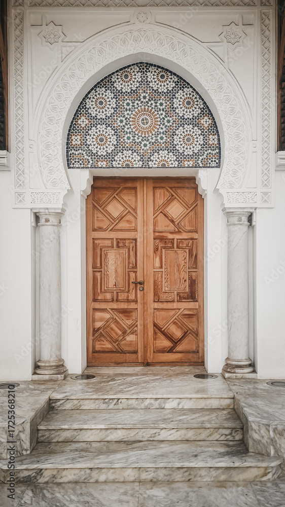Obraz premium Beautifully symmetrical wooden door framed by white arches, marble steps, and intricate zellige tilework, captured in Rabat, Morocco.