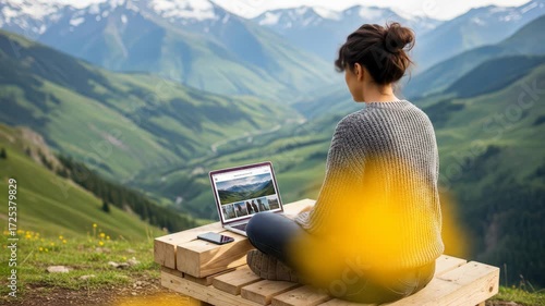 Young woman in casual sweater working on laptop outdoors in lush green mountain landscape