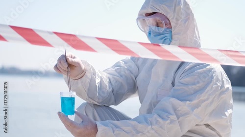 Person in protective hazmat suit and medical mask conducting water testing near lake. Environmental pollution research, contamination control, biohazard investigation, and safety inspection outdoors.