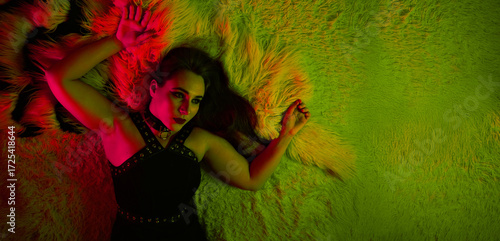 Neon portrait of woman in black dress lying on furry rug with vibrant red and lime green lighting