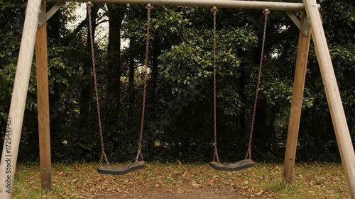Empty swing set moving gently in the breeze at a quiet park, symbolic Labor Day holiday concept, no people.
