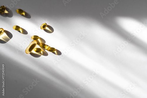 Transparent gelatin capsules with yellow oily contents containing vitamin D3 and omega on a white background with sun glare