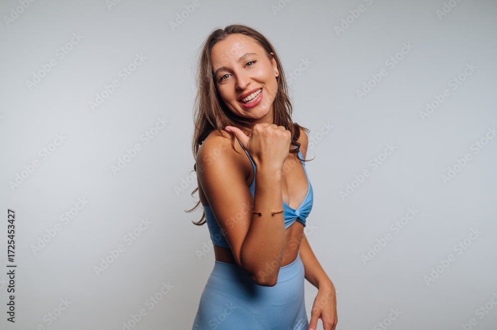 Obraz premium Smiling woman in blue activewear posing confidently against a plain background.
