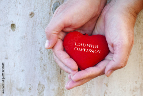 Lead with compassion -  a man holds in hands red heart with motivational text 