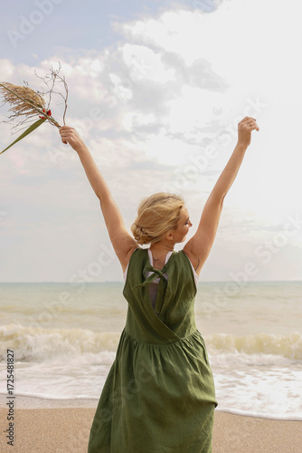 Happy woman standing on the seashore with raised arms enjoying freedom and nature