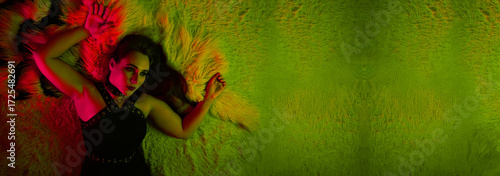 Glamorous woman lying on furry carpet under neon light – wide banner background