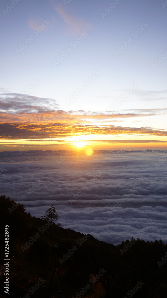 Obraz premium Breathtaking sunrise viewed from a mountaintop, with the sun glowing over a vast sea of clouds.