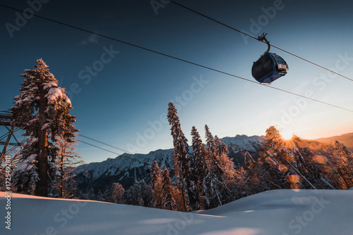 A gondola and ski lift against the backdrop of a winter landscape of mountains, trees, and an evening sunset in Krasnaya Polyana.